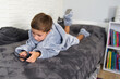 7 year old boy playing on smartphone while lying on bed