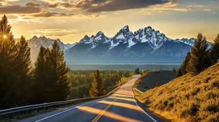 Poster - An open road leads to the Grand Teton's mountain range, rising in the distance beyond a thick pine forest. The last rays of sunlight shine on the mountain. Photo shot vertically to include more road.