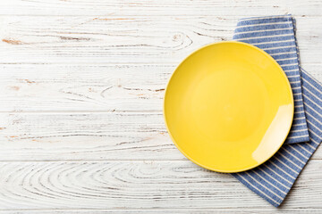 Wall Mural - Top view on colored background empty round yellow plate on tablecloth for food. Empty dish on napkin with space for your design