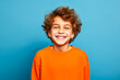 Portrait studio d'un jeune garçon souriant portant un pull orange sur fond bleu