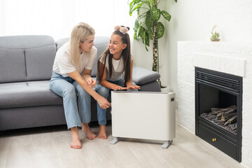 Wall Mural - Mother and child warming hands near electric heater at home