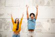 © mimagephotos - happy young couple standing by wall with arms raised