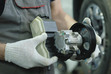 Wall Mural - A new hydraulic pump in the hands of an auto mechanic. A mechanic at a car service center monitors the serviceability of the hydraulic power steering before replacing it.