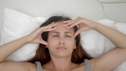 Wall Mural - Depressed young woman lies on bed closing eyes and pressing fingers to temples attractive female suffers from headache and insomnia symptom of disease