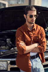 Wall Mural - handsome eye catching male model in stylish attire posing next to his car with arms crossed on chest