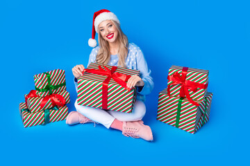 Canvas Print - Full length size photo of young blonde girl wear red santa helper hat unpacking present for new year eve isolated on blue color background