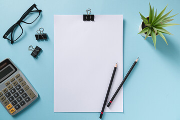 Wall Mural - Top view of blank notebook, glasses, pen, calculator and green plant on blue office desk