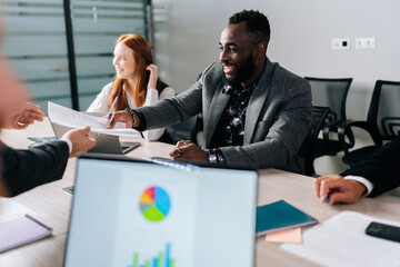 Wall Mural - Side view of cheerful African-American businessman handing over contract to business partner for signature. Business people negotiating signing of contract between companies.