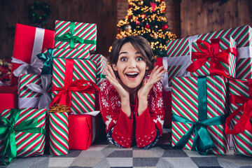 Wall Mural - Photo of pretty young girl lying floor excited hands gift pile wear trendy red sweater festive interior living room presents christmas tree