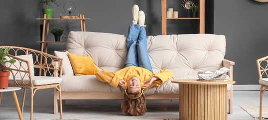 Wall Mural - Young woman with headphones listening to music on sofa at home