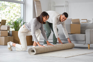Wall Mural - Happy young couple rolling carpet in room on moving day