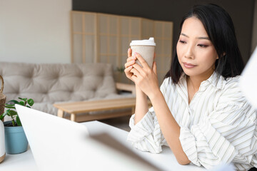 Sticker - Young Asian woman with cup of coffee working at home office