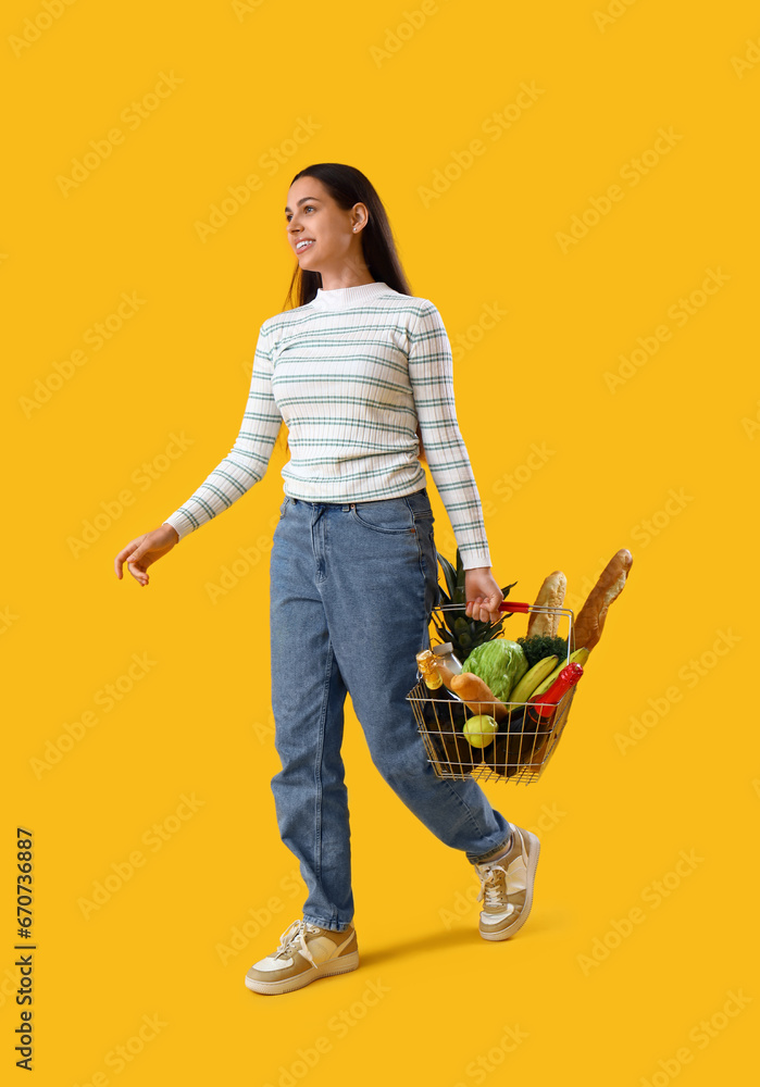 Young woman with shopping basket on yellow background