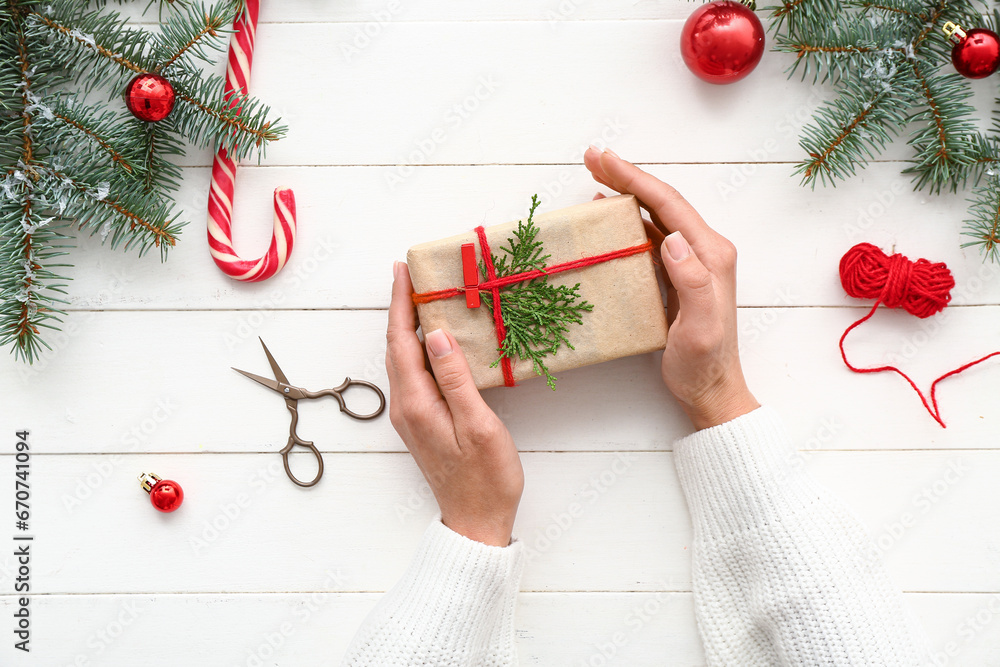 Female hands with gift box and Christmas tree branches on white wooden background