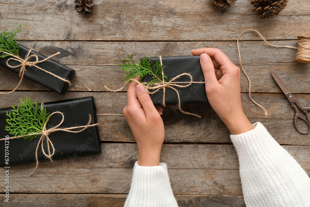 Female hands with Christmas gift boxes and coniferous branches on wooden background