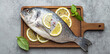 Raw uncooked fish dorado with lemon and fresh basil on wooden cutting board with knife on rustic stone background top view, cooking healthy fish dorado concept