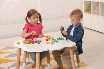 Wall Mural - Little children playing with wooden pieces and string for threading activity at white table indoors. Developmental toys