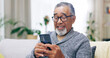 © Charlize D/peopleimages.com - Senior man, happy and phone on couch for texting, reading or thinking for contact in home living room. Elderly person, smartphone and smile for notification, social media app and relax on lounge sofa