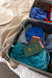 Sun hat, passports and clothes in suitcase in sunny bedroom at home