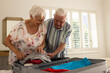 Happy caucasian senior couple packing suitcase in sunny bedroom at home