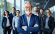 © Kowit - Portrait of successful senior businessman standing with his arms crossed businessman and businesswoman over big group of businesspe. Caucasian male entrepreneur in suit looking at camera with a smile.