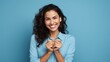 Hispanic woman standing over blue background smiling lovingly and making heart symbol shape with hands. romantic concept. I love you.
