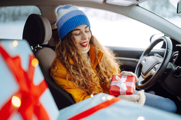 A beautiful woman driving a car carries New Year's gifts along a snowy road. Happy woman giving gifts. On the eve of the winter holidays, preparation. Shopping concept.