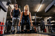 © dusanpetkovic1 - A female personal trainer is looking at the female bodybuilder who is doing deadlifts in a gym.