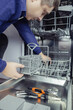 © Siniehina - Dishwasher repair. A service center representative diagnoses and repairs a dishwashing machine at home. Specialist in working with home appliances. Call a technician to your home. Close-up
