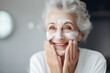 © ribalka yuli - A beautiful senior woman applies cream or mask to her face. Self care concept in old age