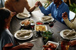 Hands of religious African American family members during Thanksgiving pray by served table with appetizing homemade food and drinks