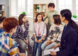 © Studio Romantic - Group of elementary school children together with their teacher sitting in a circle in the classroom and discussing a sad story from the book that they have read today