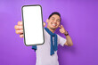 © Bangun Stock Photo - Cheerful young Asian man pointing index finger at empty smartphone screen isolated on purple background. Advertising new mobile app, mockup concept