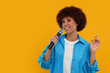 © New Africa - Curly young woman with microphone singing on yellow background, space for text