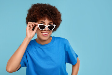 Poster - Happy young woman in stylish sunglasses on light blue background. Space for text