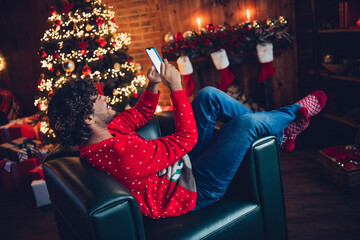 Full length photo of relaxing arab guy spending winter holidays at home lying comfortable couch and typing phone order presents for xmas