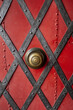 Close up of an old metal red door with diagonal iron decorative strips and rivets.