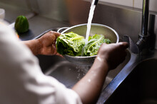 African american male chef washing vegetables in sink in restaurant kitchen