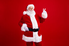 Photo Of Cheerful Funky Retired Man Santa Claus Showing V-sign Celebrate Christams Time Isolated On Red Color Background