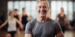 Grey haired man smiling, enjoying yoga class, blurred women in the background