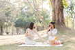 © wichayada - Two beautiful LGBT young women in casual clothes and summer hats Carefree woman having a picnic outside Positive model sitting on the grass eat fruit and cheese Take a selfie. LGBT concept