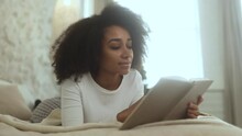 Relaxed young curly woman reading book literature laying on bed at cozy home Calm relaxed african american female enjoying weekend leisure time alone indoors