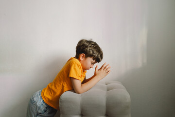 Wall Mural - A boy in an orange T-shirt prays at home. Reading the Holy Bible. Concept for faith, spirituality and religion. Peace, hope.