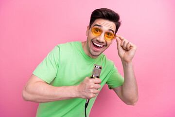 Canvas Print - Portrait of crazy young singer man wear green t shirt touch sunglasses holding microphone concert isolated on pink color background