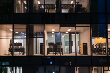 Business building with office and workspaces with desks, laptops and armchairs at night. Work, career and finances