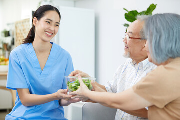 Wall Mural - nurse or caregiver serving vegetables in a bowl to senior couple on sofa