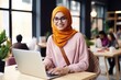© FoxTok - Attractive Muslim girl in hijab smiles and works on modern laptop at table in cafe on the street. Student watching lectures online, video call, young business lady freelancer