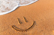 Smiley drawn on the sandy beach, travel and vacation concept. sea wave, top view of the sandy beach. Face in the sand at the beach