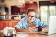 © Geber86 - Happy young woman looking at a smartphone while going over paperwork in the kitchen