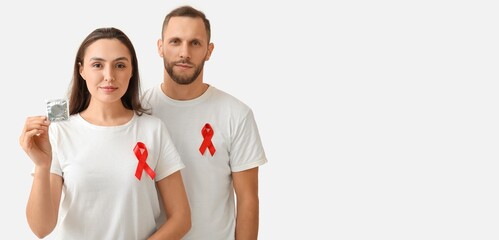 Wall Mural - Young couple with red awareness ribbons and condom on light background with space for text. Banner for World AIDS Day